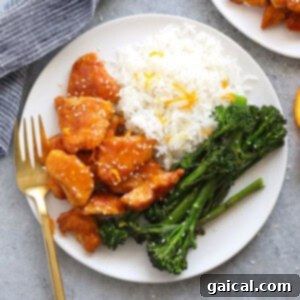 A bowl of healthy orange chicken garnished with sesame seeds and green onions.