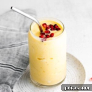 A vibrant, creamy mango smoothie in a glass, garnished with a few pomegranate seeds on top, ready to be enjoyed.