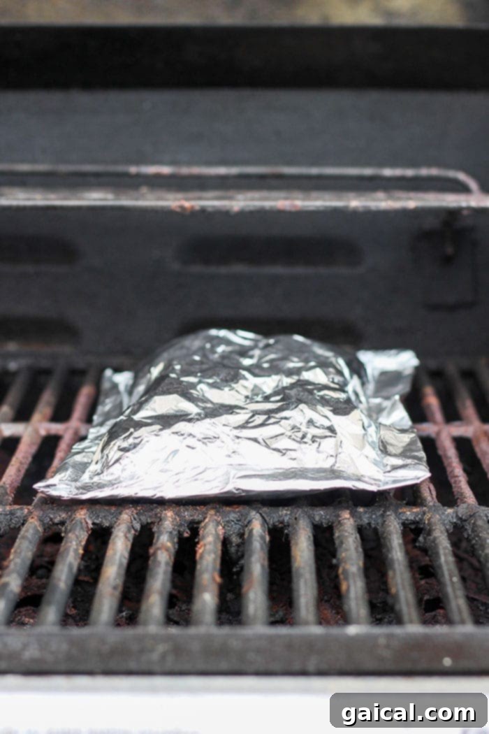 Foil pack of seasoned potatoes cooking directly on a hot grill