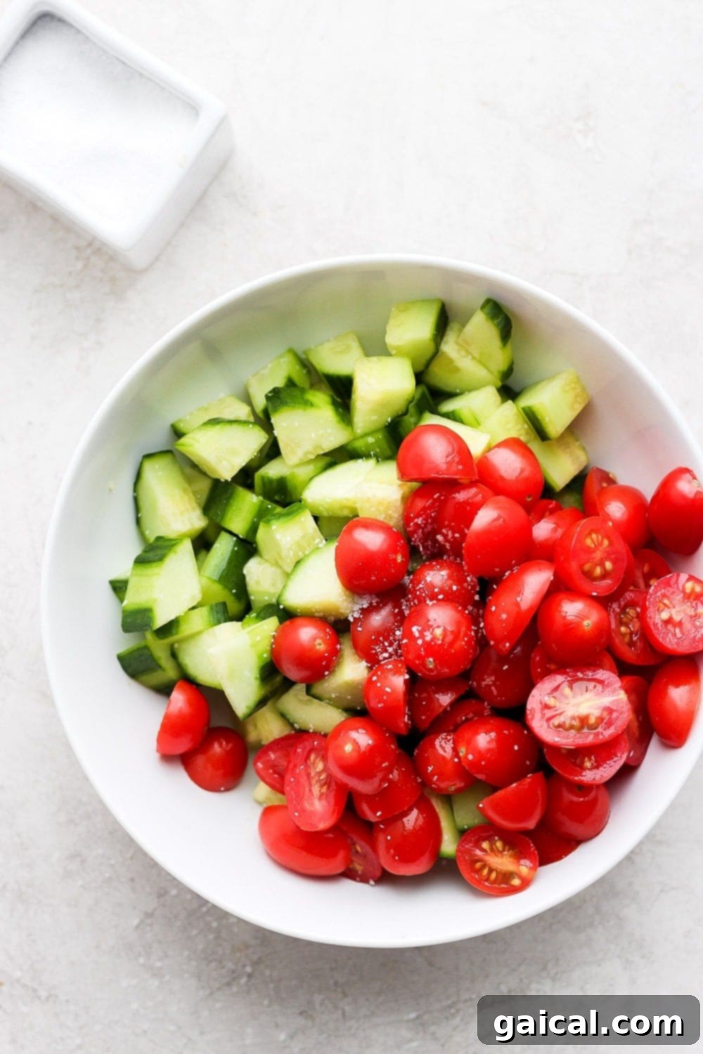 Close-up of fresh, chopped English cucumbers and halved sweet cherry tomatoes in separate bowls, ready for the crucial moisture-draining step.