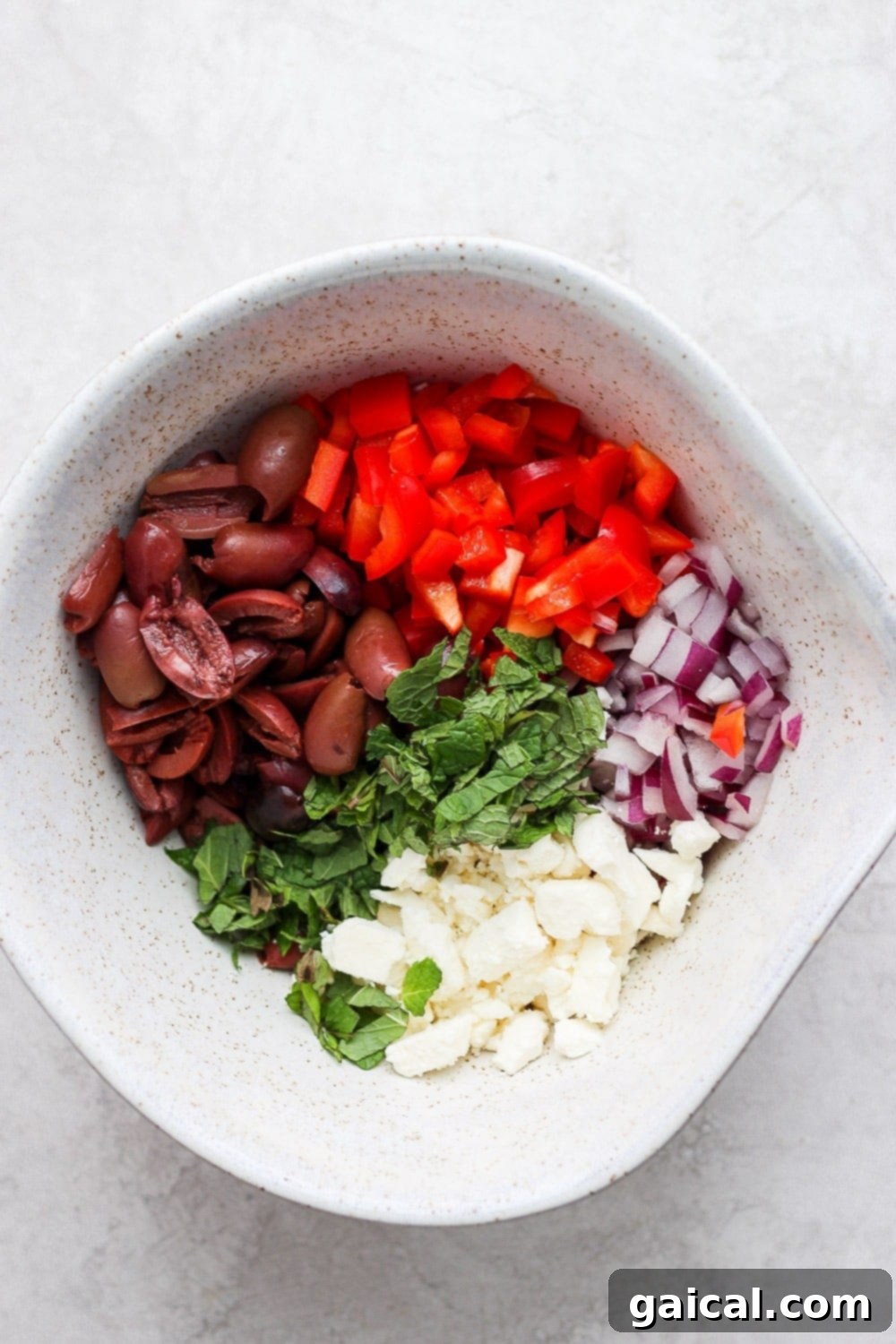 All the fresh ingredients for the Greek salad, including drained cucumbers and tomatoes, red onion, bell pepper, kalamata olives, and feta, artfully arranged in a large mixing bowl before the dressing is added.