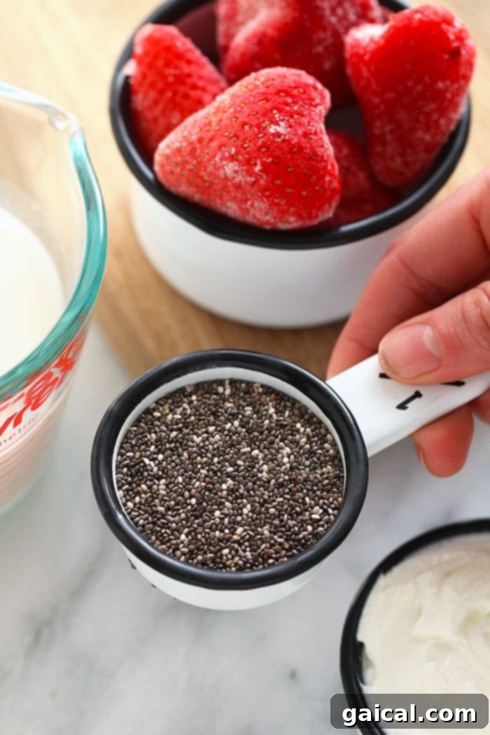 Measuring cup filled with chia seeds next to a bowl of fresh strawberries, ready for blending.