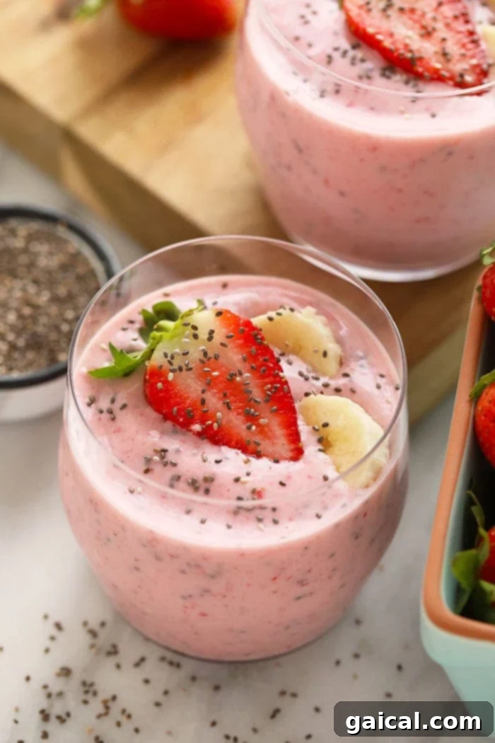 A beautifully presented creamy strawberry chia seed smoothie in a tall glass, garnished with a slice of fresh strawberry and a sprinkle of chia seeds.