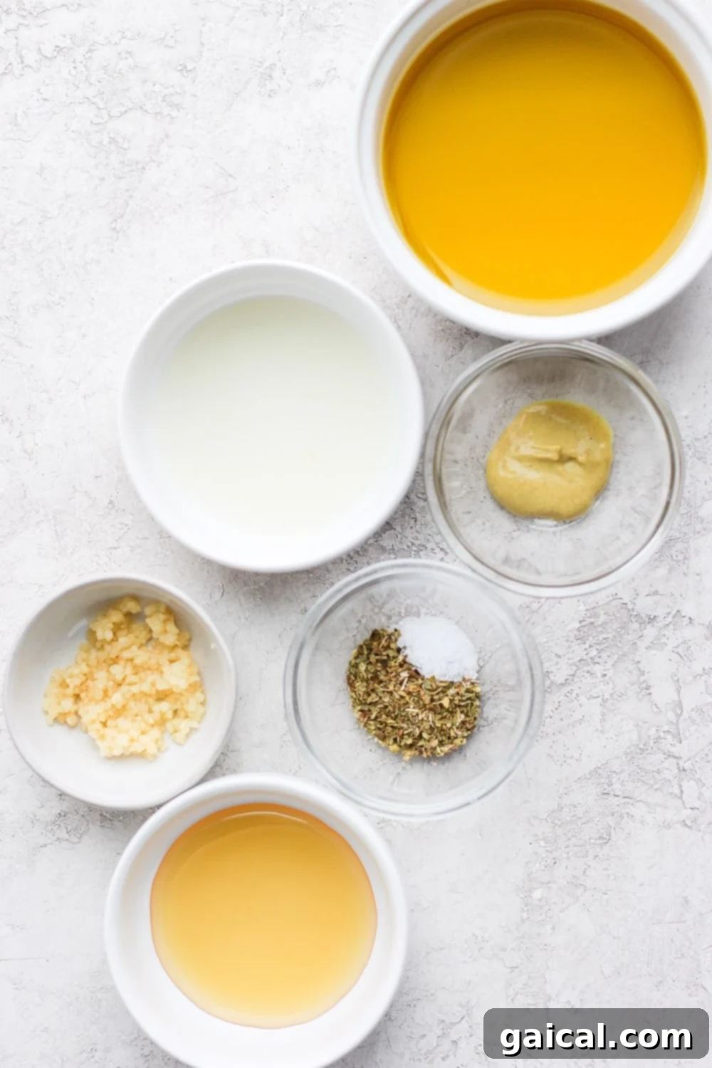 A collection of fresh, individual ingredients neatly arranged for making Greek salad dressing: olive oil, white wine vinegar, minced garlic, honey, lemon, Dijon mustard, dried oregano, and salt, ready to be combined into a delicious dressing.