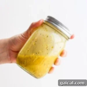 a hand holding a jar of Greek salad dressing, ready to be poured.