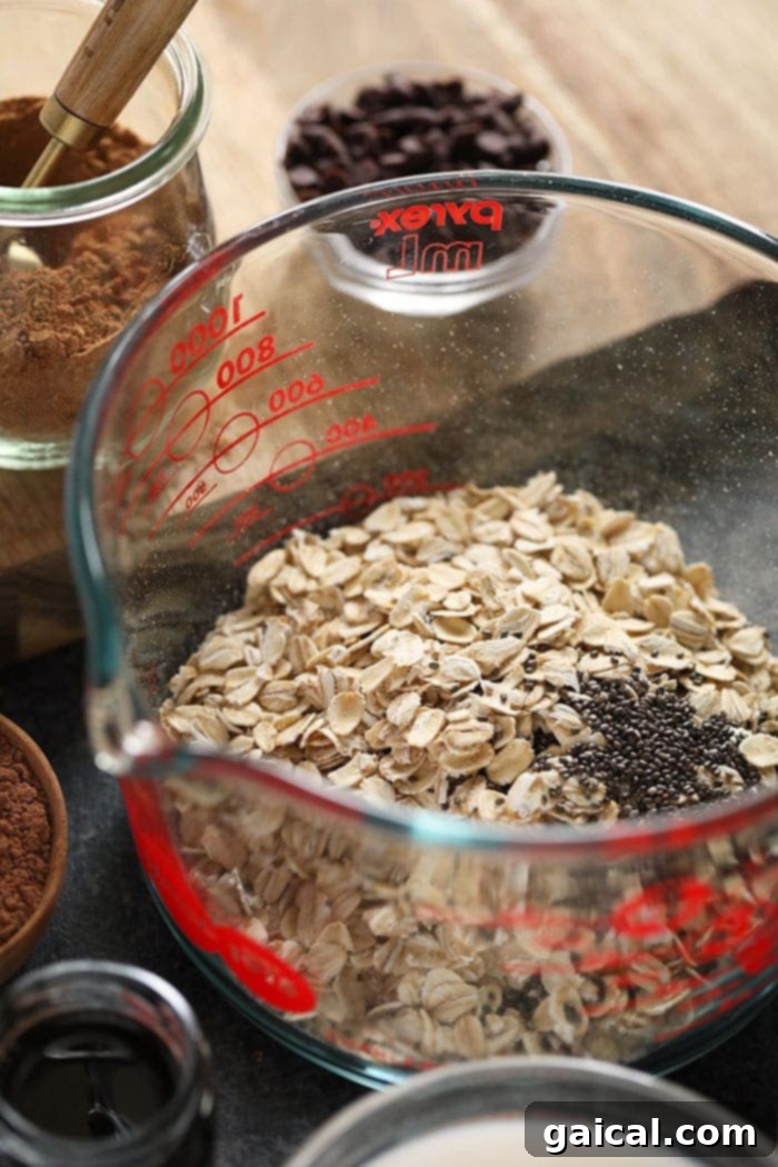 Close-up shot of dry rolled oats and chia seeds being mixed in a bowl, illustrating the starting point of making overnight oats.