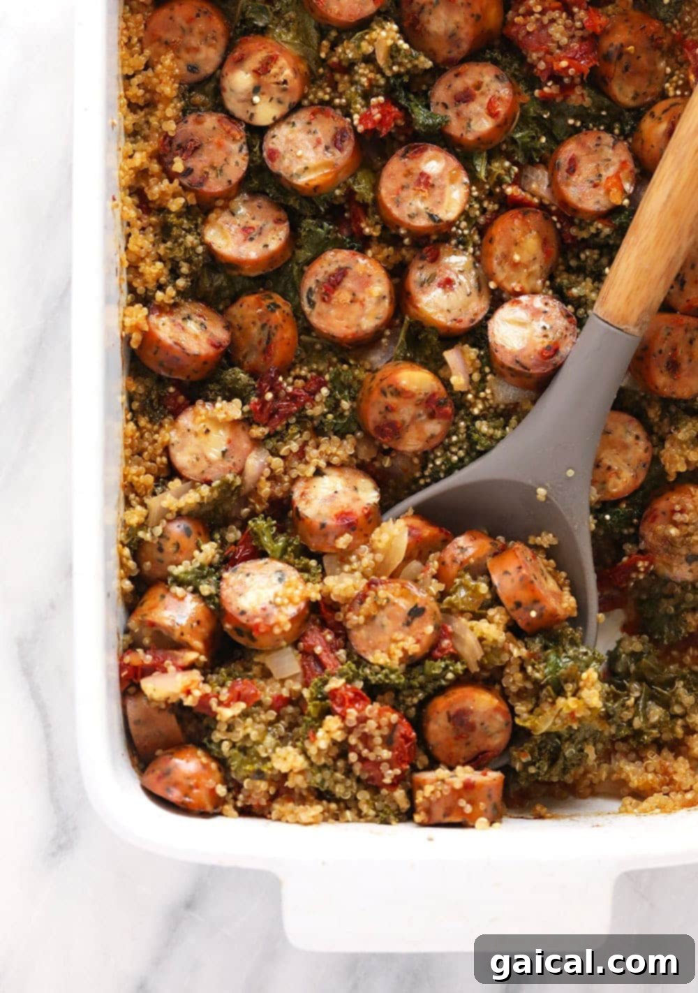 A large serving of Italian chicken sausage quinoa casserole, fresh from the oven, with a serving spoon ready to dish out.