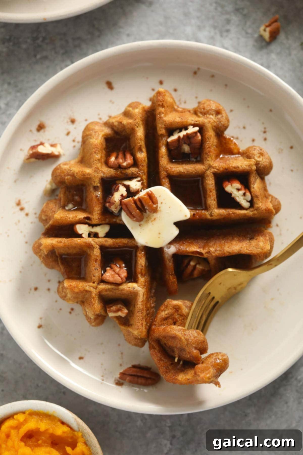 Got pumpkin? Make these delicious pumpkin gluten free waffles recipe! It's made with simple ingredients and pumpkin pie spice. A single gluten-free pumpkin waffle on a white plate, ready with a fork, showing its delightful texture.