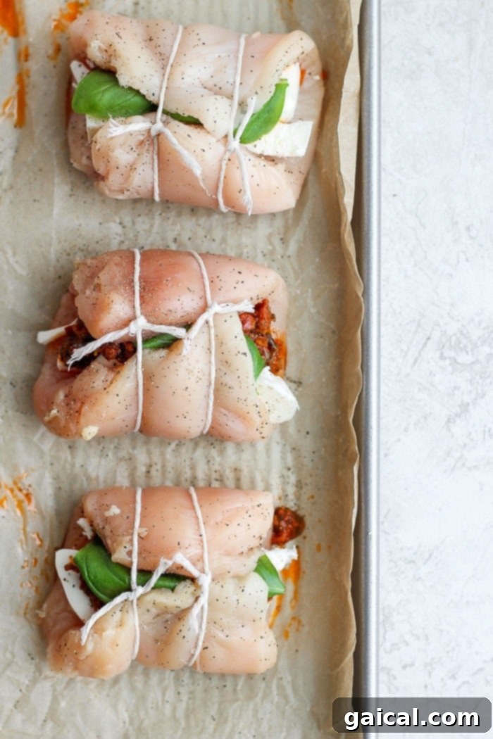 This stuffed chicken breast is a delicious weeknight dinner meal, easy to prepare and full of flavor. Caprese stuffed chicken breast rolled up and tied with cooking twine on a baking tray.
