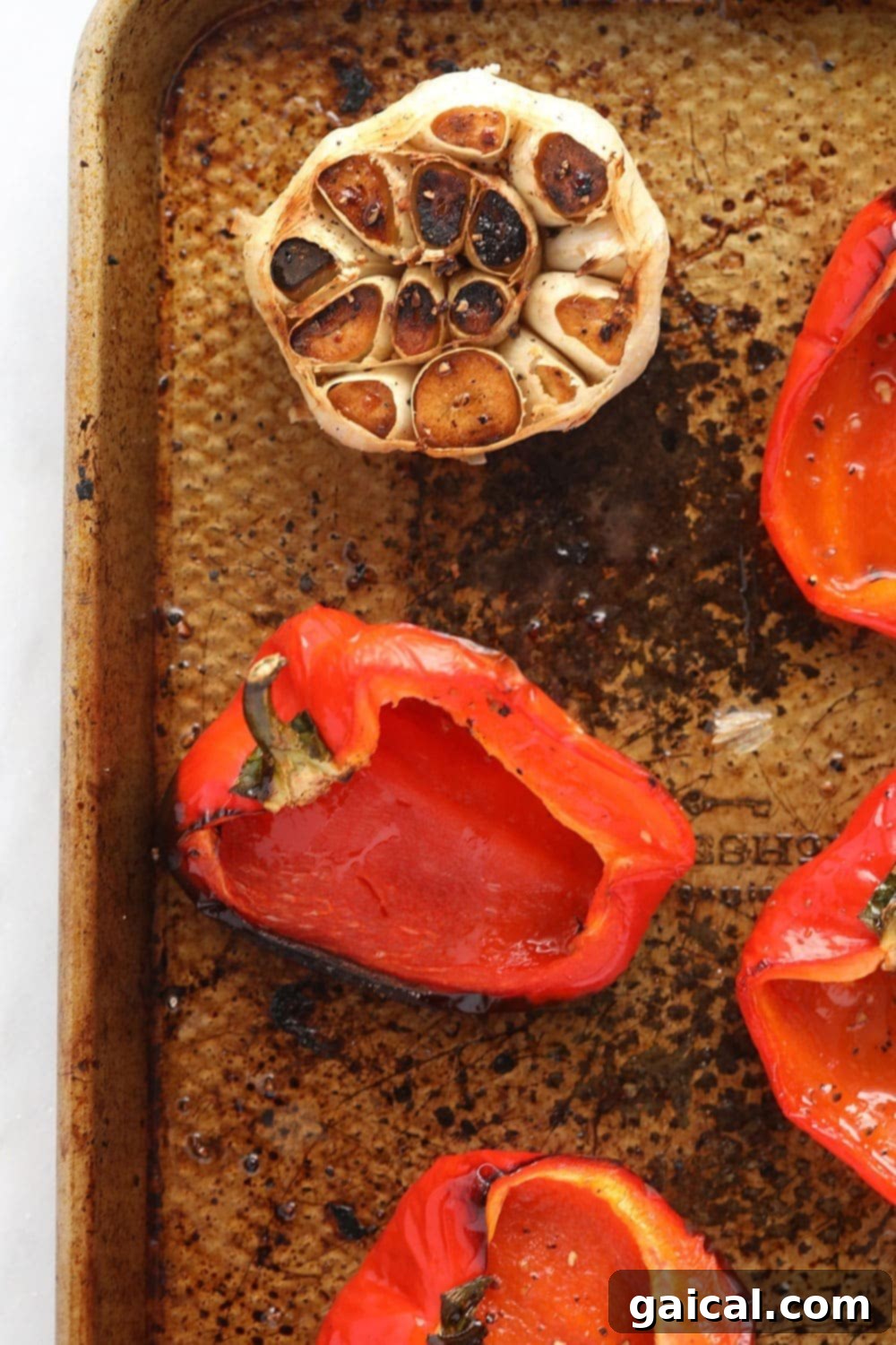 Red peppers and whole garlic cloves arranged on a baking sheet, ready for roasting.