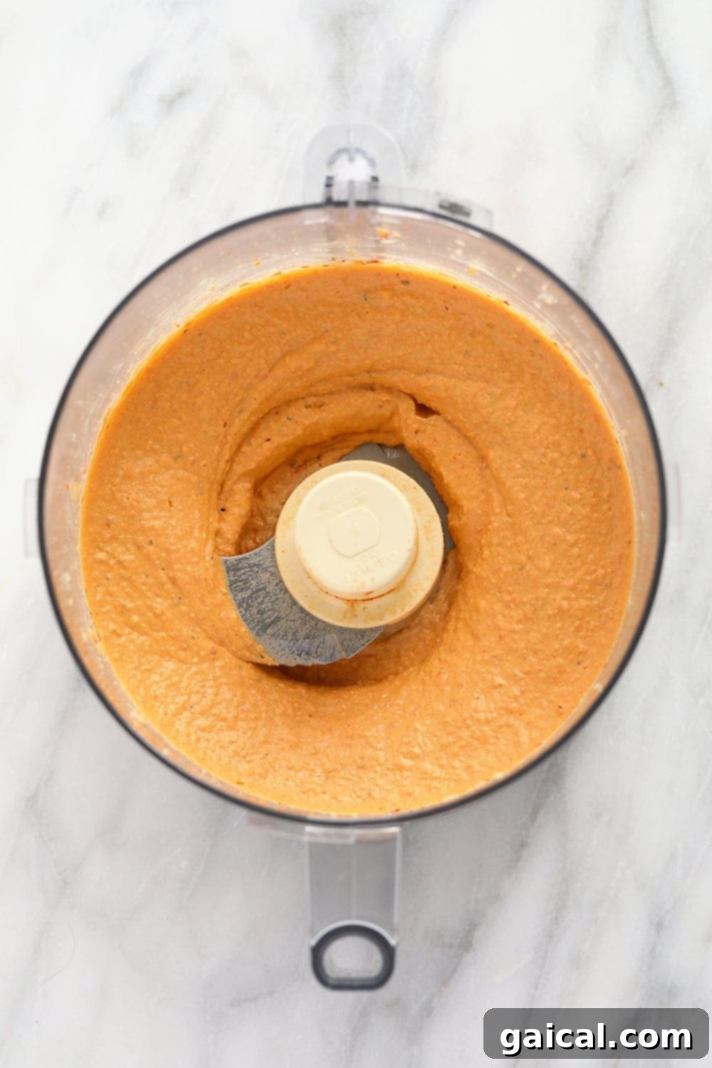 Perfectly blended roasted red pepper hummus swirled in a food processor bowl, ready to be served.