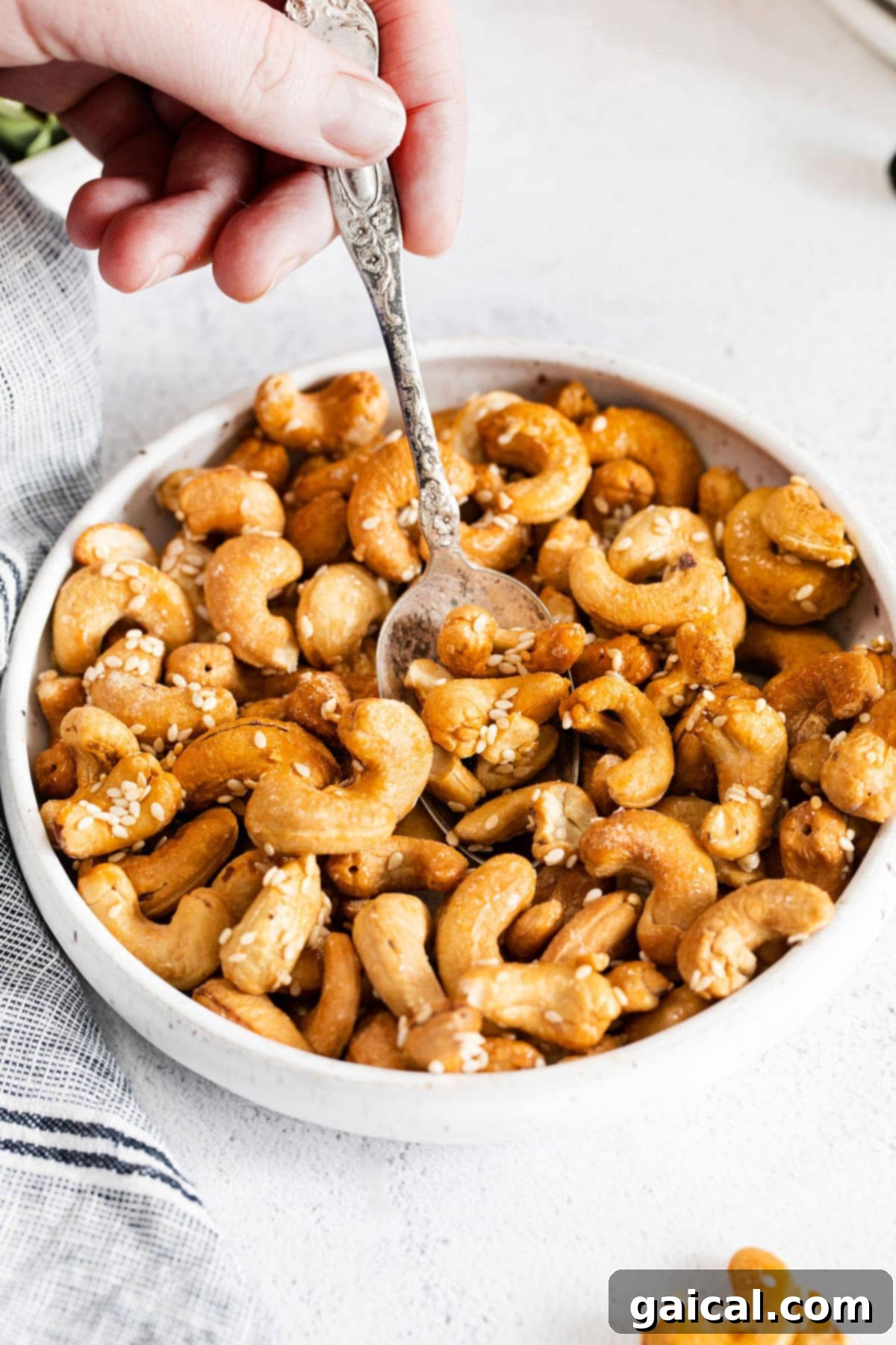 A bowl of golden roasted cashews with sesame seeds and a spoon, ready to be enjoyed as a healthy snack or salad topping.