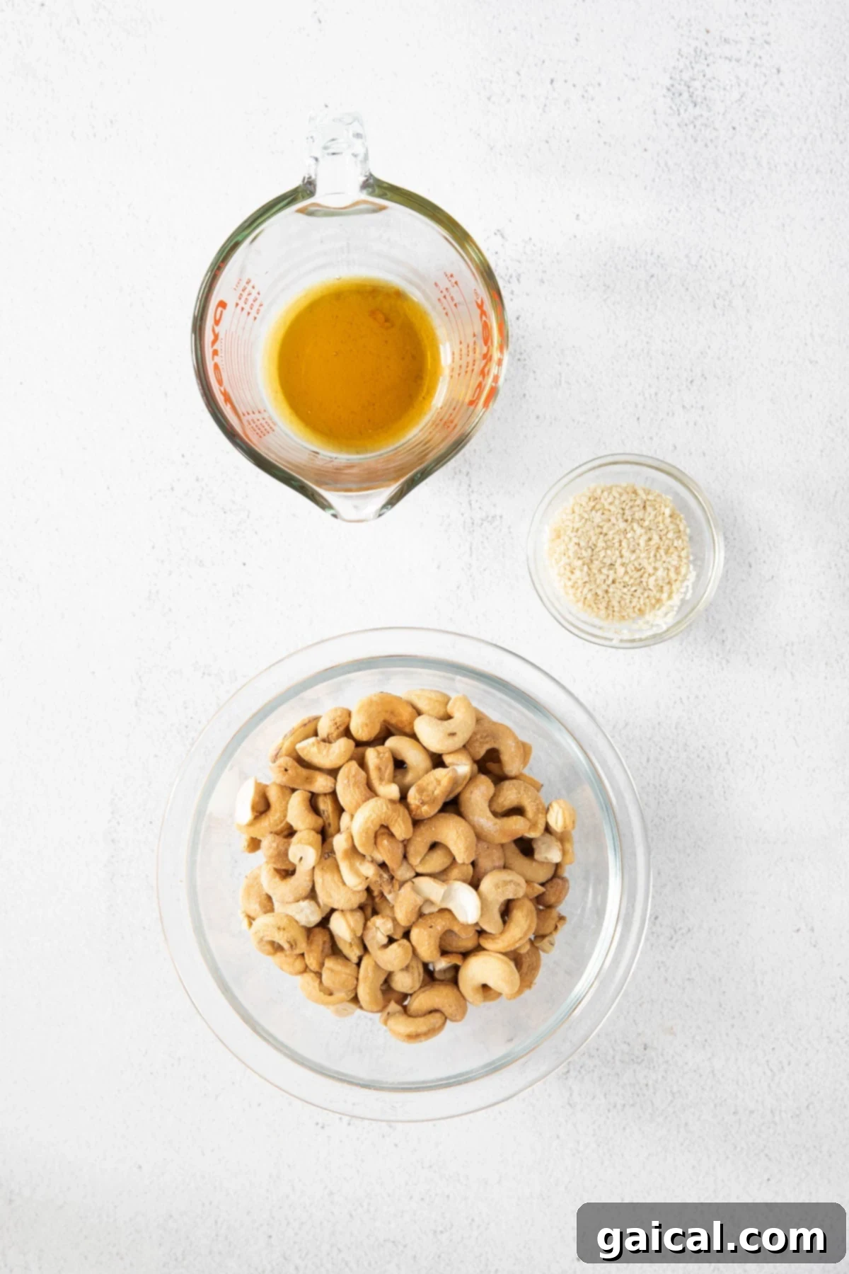 Close-up of maple syrup, raw cashews, and sesame seeds arranged on a surface, showcasing the simple ingredients for roasted cashews.