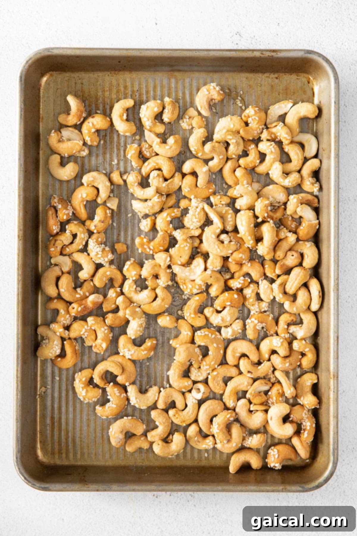 Raw cashews spread evenly on a parchment-lined baking sheet, preparing for the roasting process.