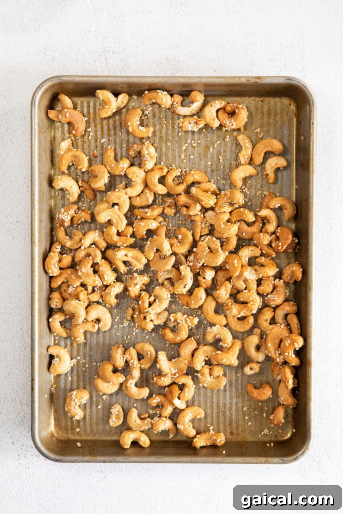 A baking sheet filled with perfectly roasted cashews, glistening with maple syrup and generously coated in sesame seeds, fresh out of the oven.
