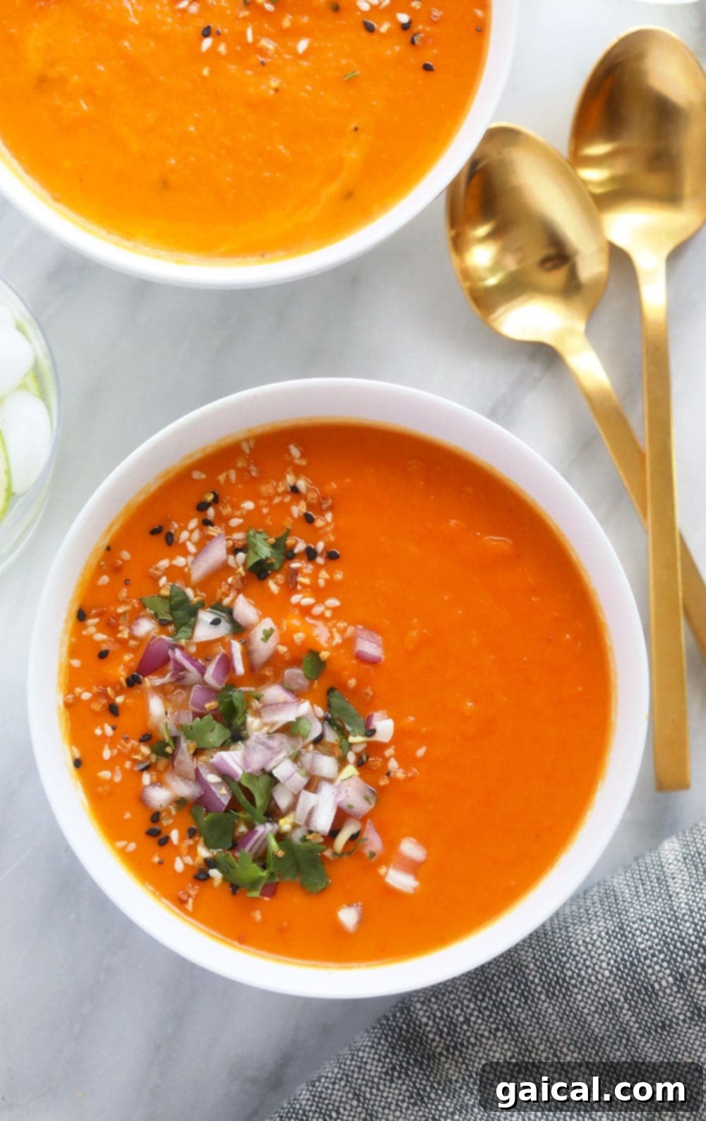A large bowl of Instant Pot Sweet Potato Carrot Ginger Soup, garnished with diced red onion and fresh herbs.