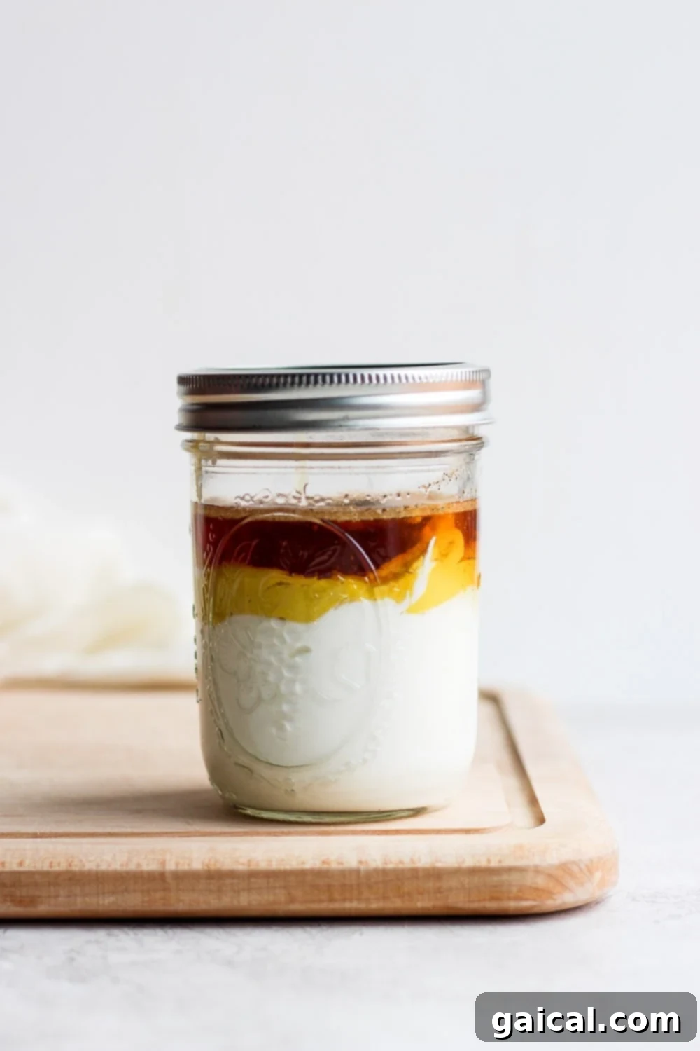 Effortless Honey Mustard Delight 4 Stacked ingredients for homemade honey mustard dressing in a mason jar on a wooden cutting board.