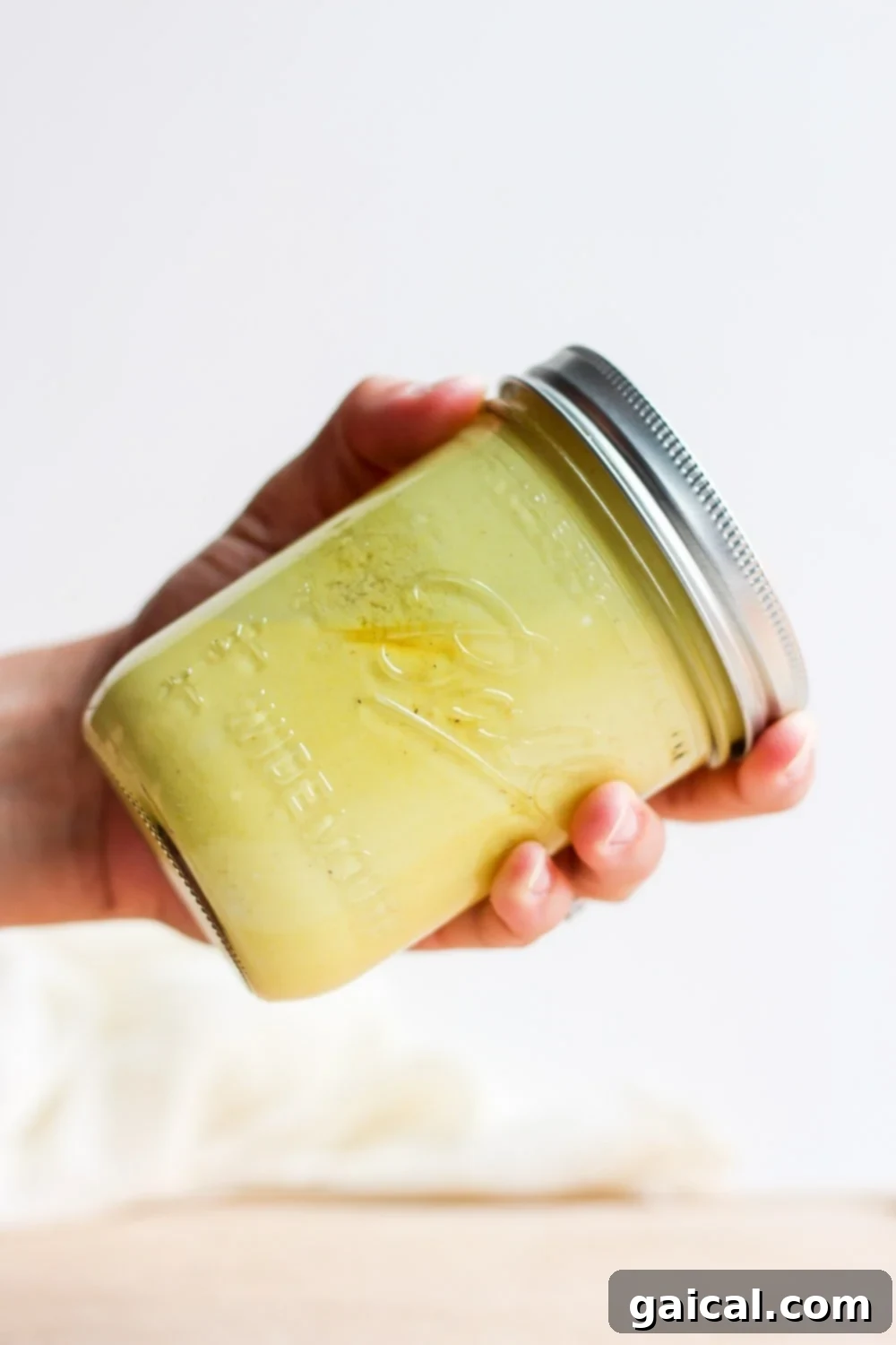 Effortless Honey Mustard Delight 5 A hand shaking a glass jar filled with homemade honey mustard dressing to mix the ingredients.