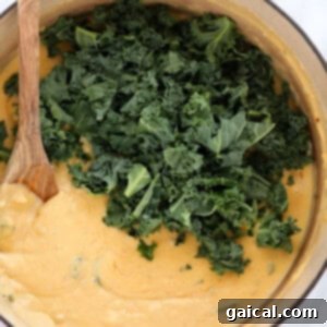 Fresh kale being mixed into the creamy cheese sauce for the mac and cheese.