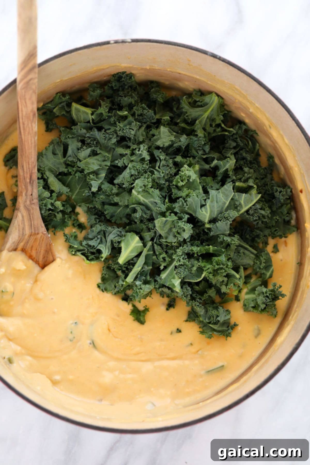 Wholesome Quinoa Mac 5 Wilted fresh kale being mixed into the creamy, bubbling cheese sauce in a Dutch oven, ready for the quinoa.