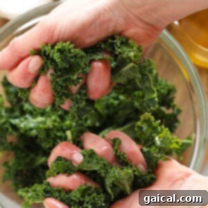 Hands massaging fresh kale leaves with olive oil and salt.