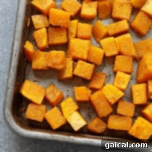 Cubed butternut squash seasoned and spread on a baking sheet, ready for roasting.