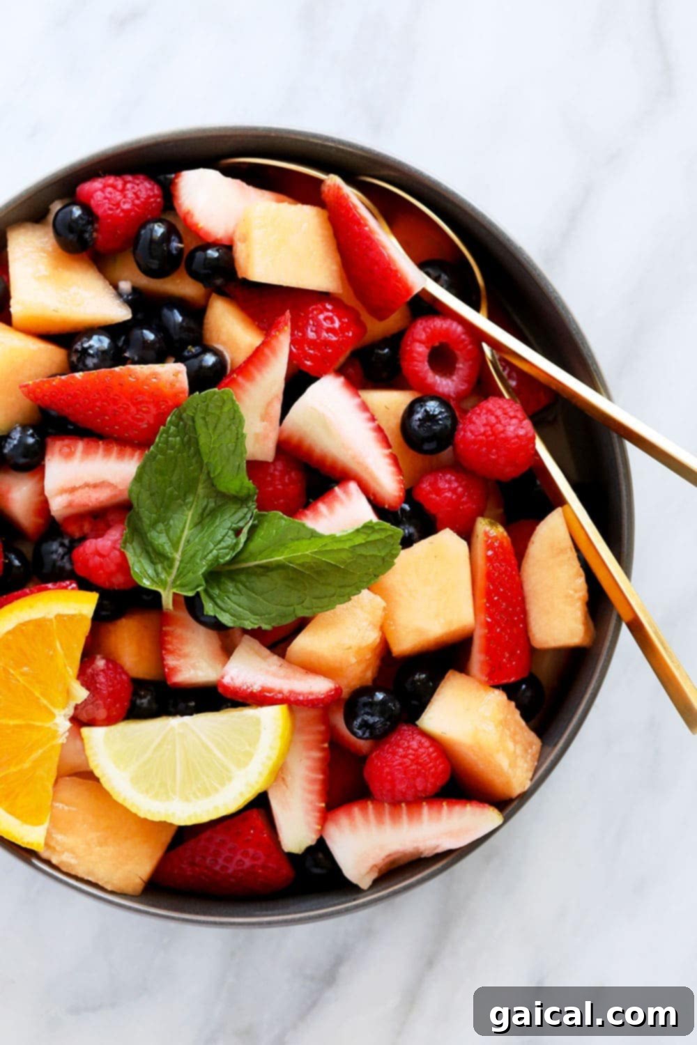 This fruit salad recipe makes for a healthy and flavorful summer side dish or kid-friendly snack! Made from fresh fruit and a 2-ingredient homemade dressing, this fruit salad is ready to enjoy in 15 minutes tops! beautiful fruit salad recipe in a bowl topped with fresh mint