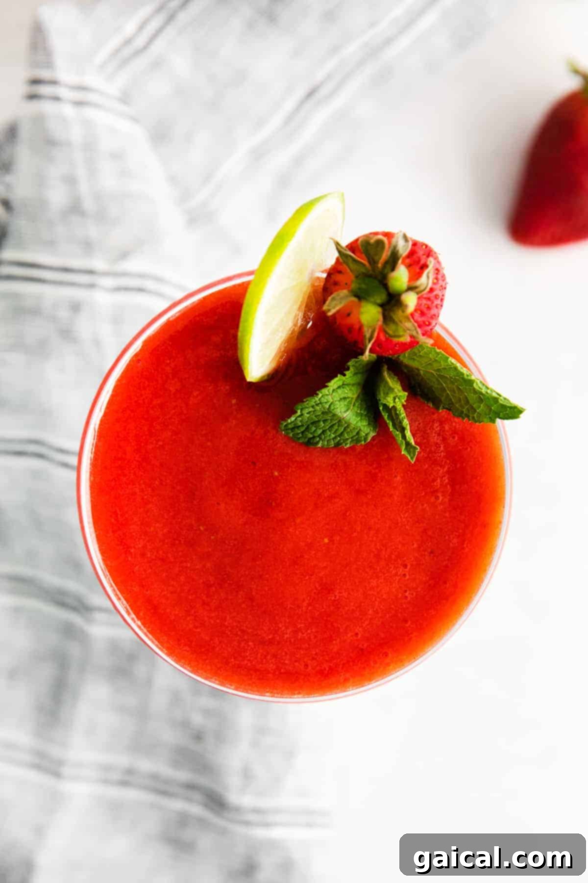 A close-up of a perfectly poured strawberry daiquiri in a glass, garnished with lime and a fresh strawberry.