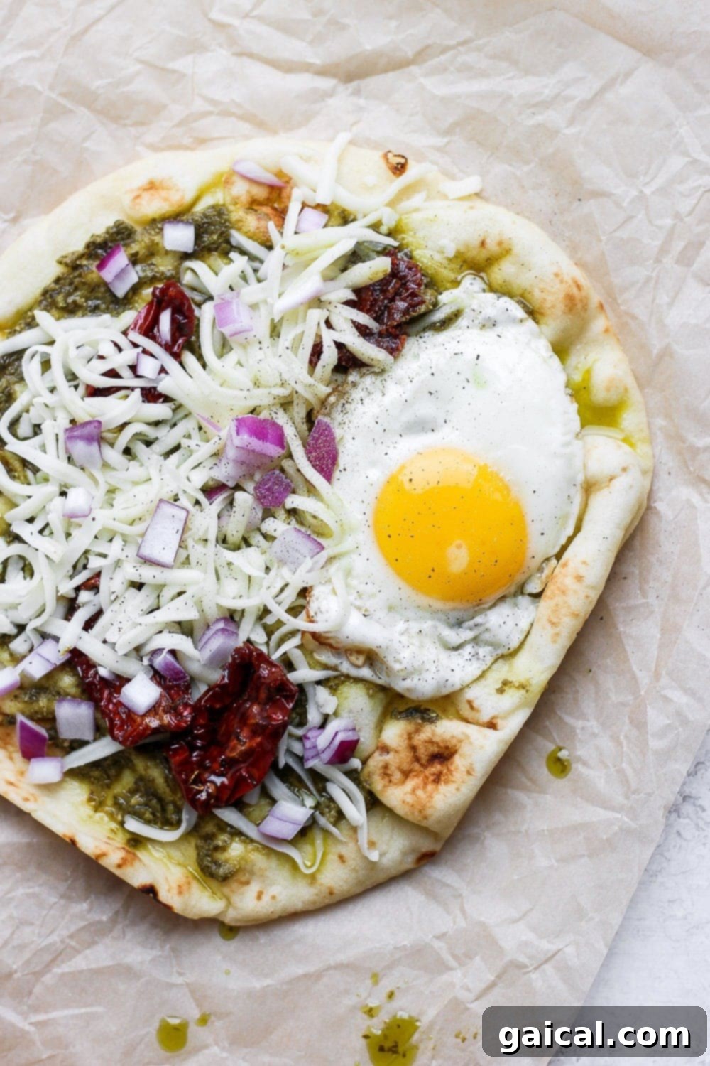 Naan Breakfast Bake 5 Completed pesto naan pizza featuring sun-dried tomatoes, cheese, and a perfect fried egg.