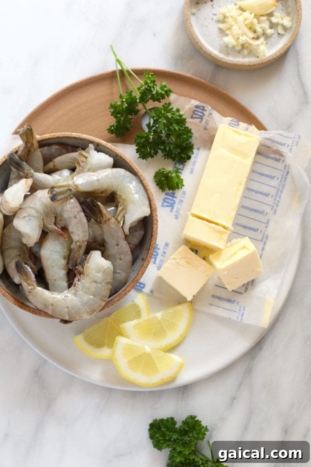 Fresh, raw extra-large shrimp next to a stick of butter, poised for sautéing in a skillet, showcasing the simple ingredients.