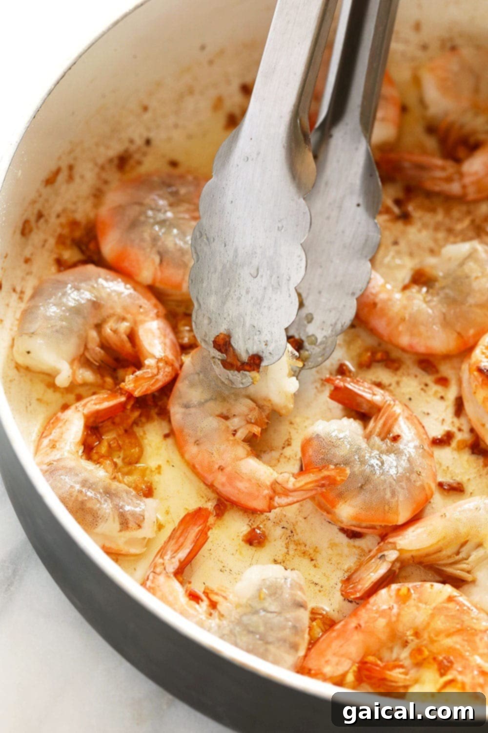 Garlic butter shrimp sizzling in a hot skillet, being skillfully flipped with tongs as it cooks to a perfect pink hue.