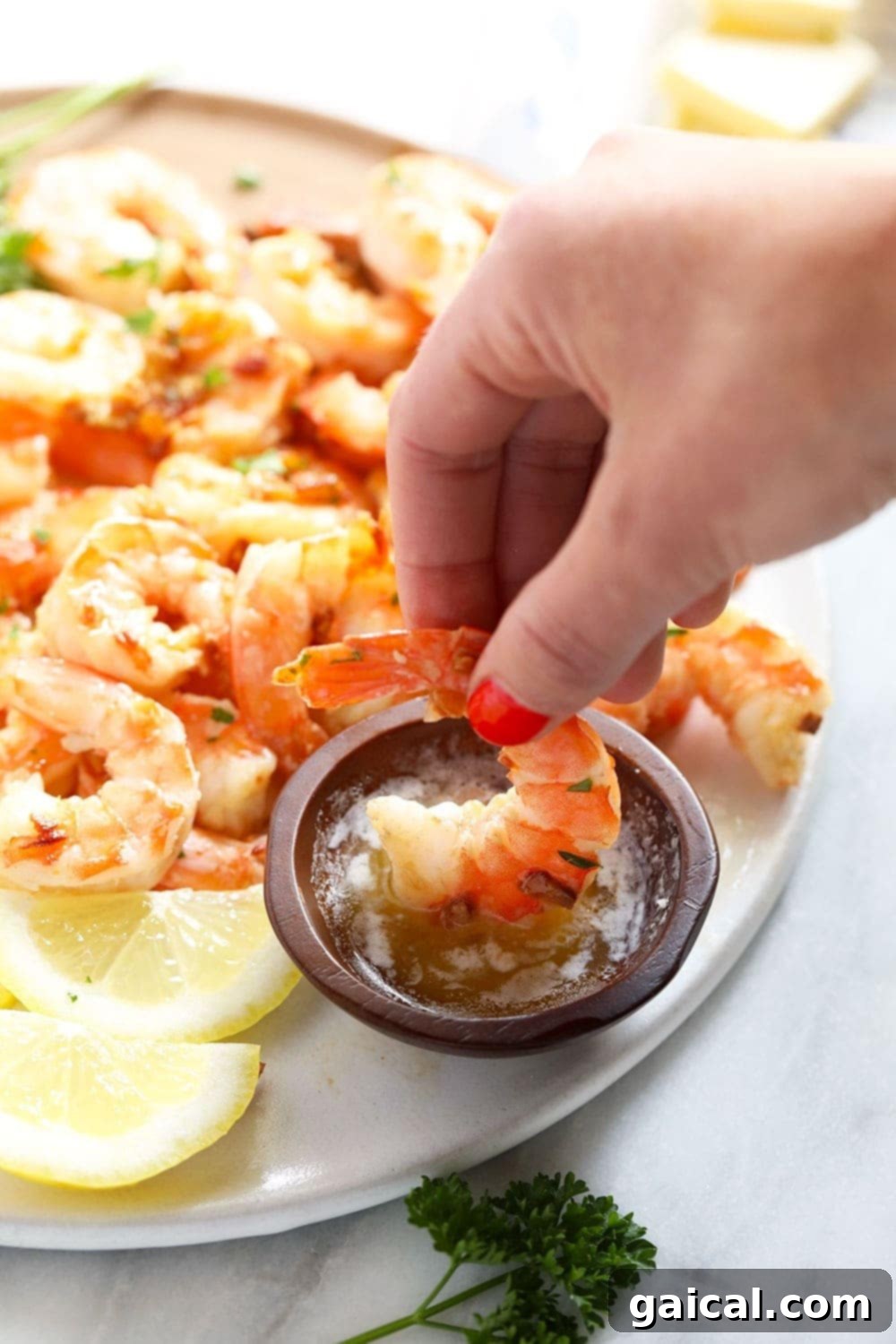 A close-up shot of a single piece of garlic butter shrimp being dipped into a small bowl of rich, melted butter.