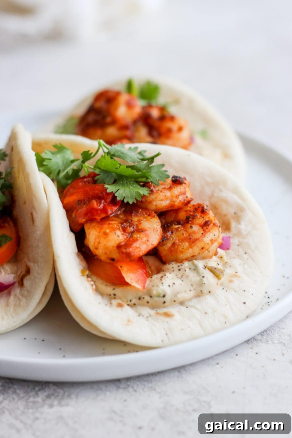 Three perfectly assembled shrimp tacos in street taco tortillas, bursting with colorful ingredients.