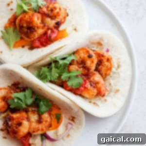 Three shrimp tacos on a white plate, garnished with fresh cilantro.