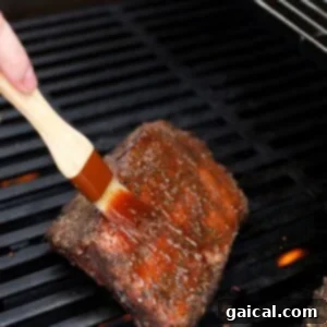 Brushing barbecue sauce onto sous vide ribs on a barbecue grill.