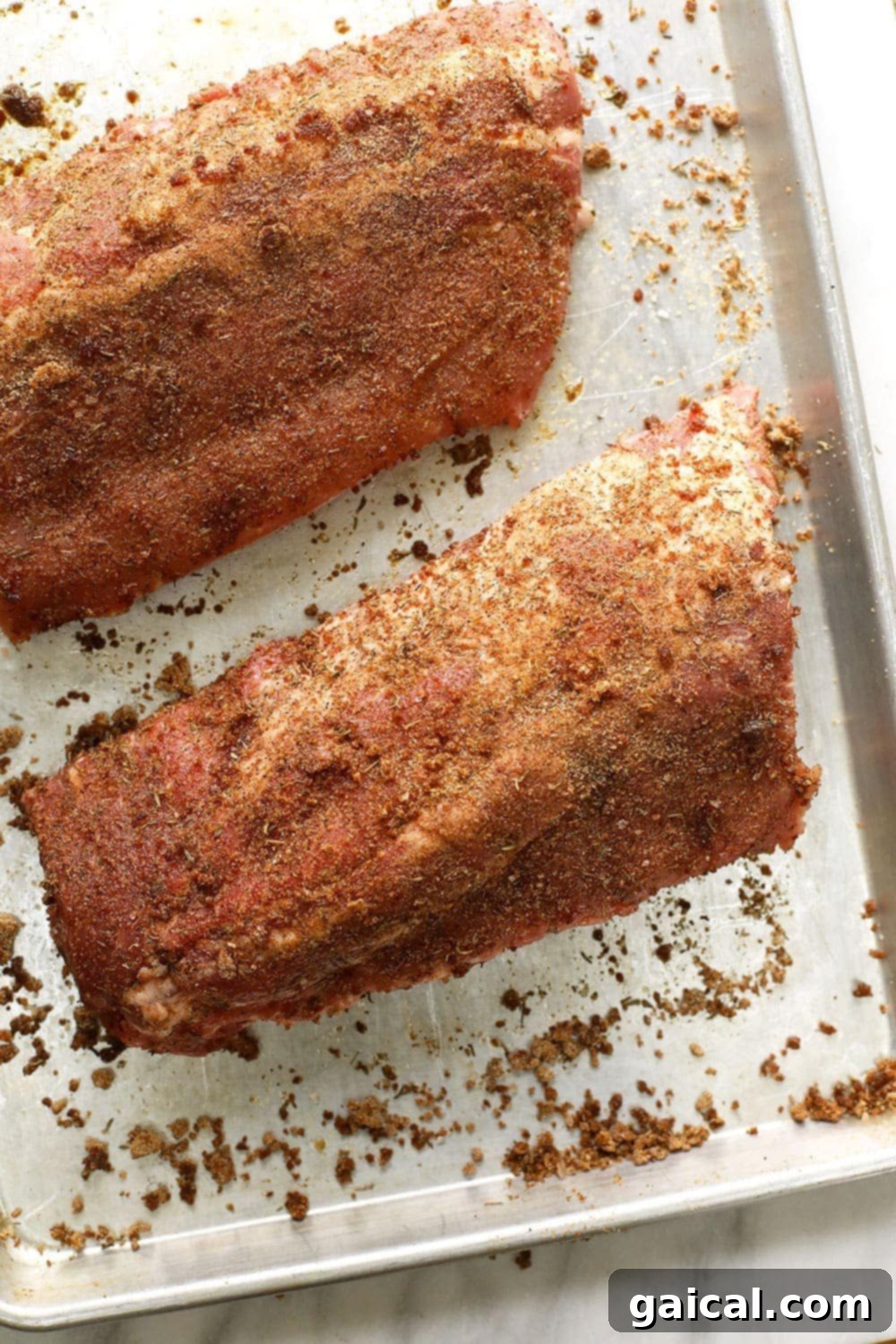 These bbq ribs are rubbed with a smokey dry rub, cooked in a sous vide bath for 24 hours, slathered with BBQ sauce, and then grilled to perfection. Dry rubbed sous vide ribs on a baking sheet.
