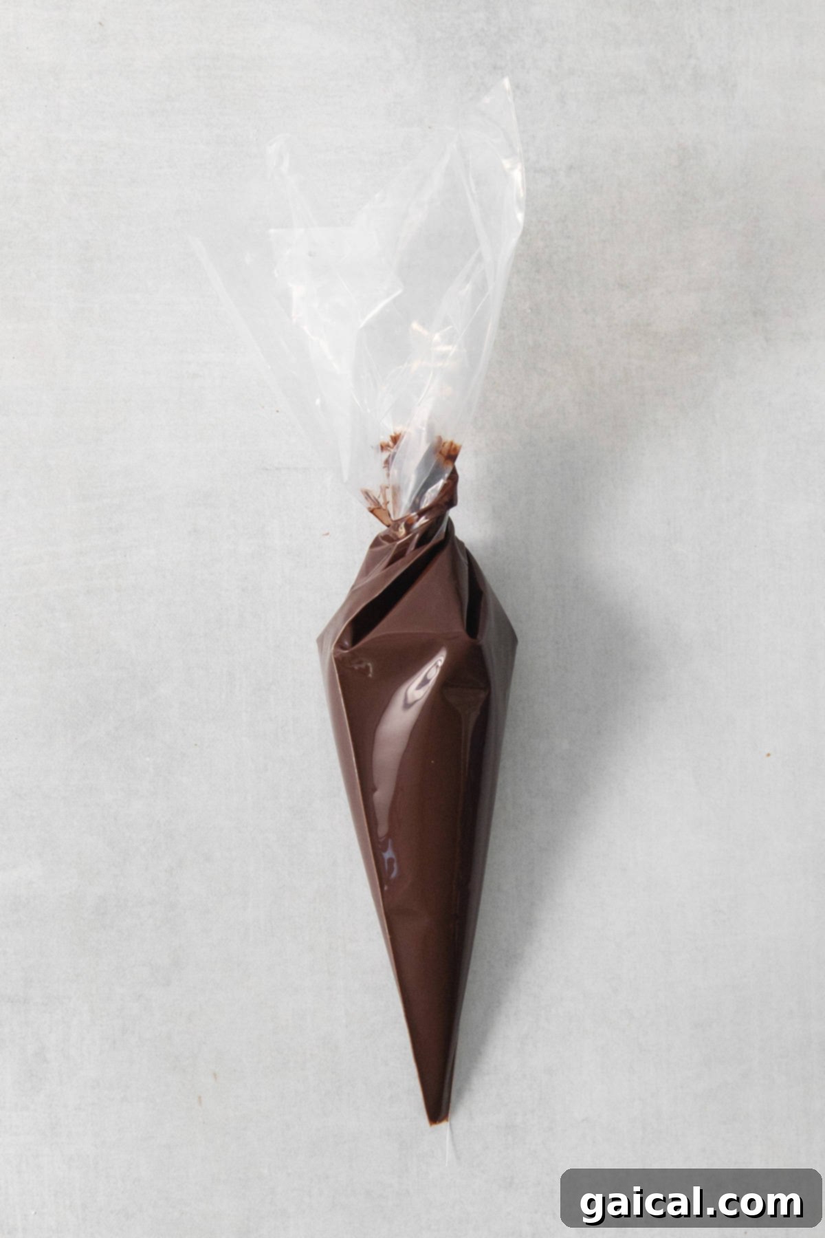 Quick & Easy Homemade Vegan Chocolate Chips 4 A cone of chocolate wrapped in plastic on a concrete surface.