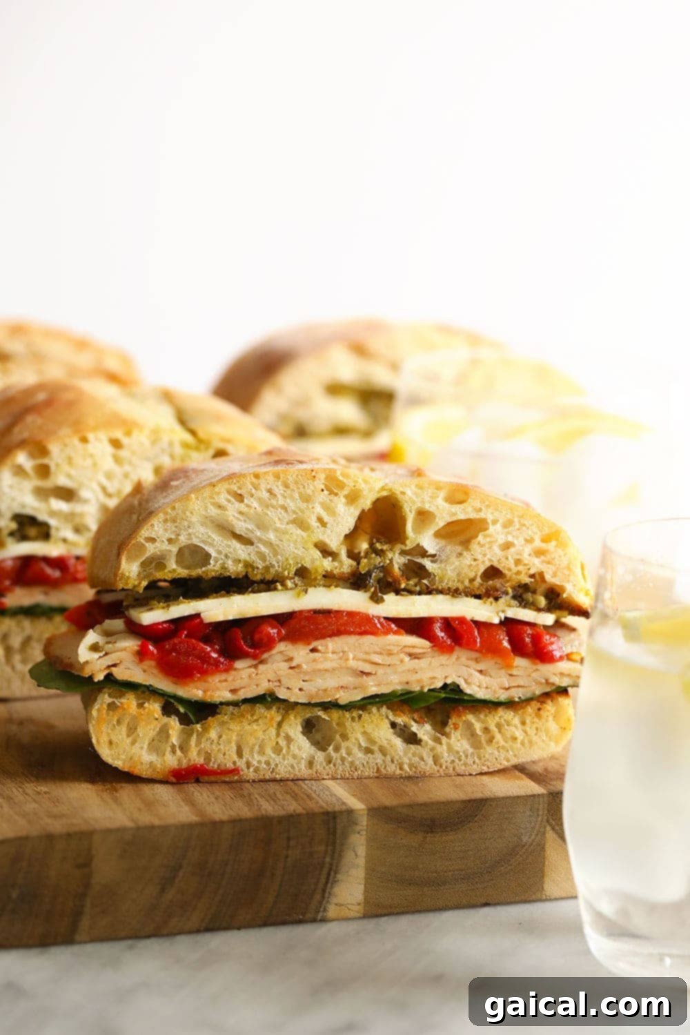 A perfectly grilled turkey pesto sandwich on a wooden cutting board, with vibrant green pesto and roasted red peppers visible
