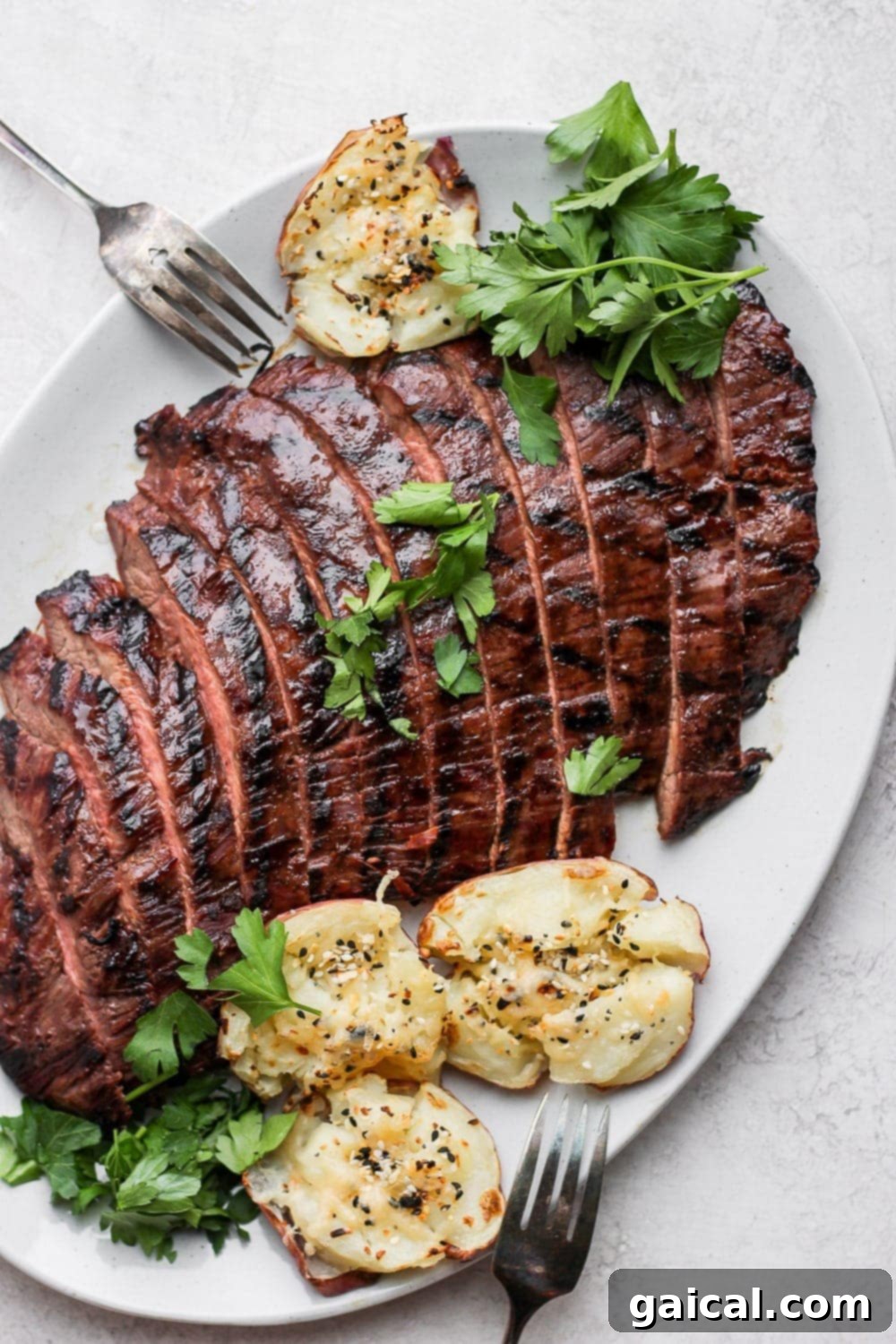 Add this grilled flank steak recipe to the menu this summer! It's tenderized, marinated, and grilled, making this easy grilled flank steak so tender and delicious. Grilled flank steak on a plate with smashed potatoes and fresh parsley, ready to be served.