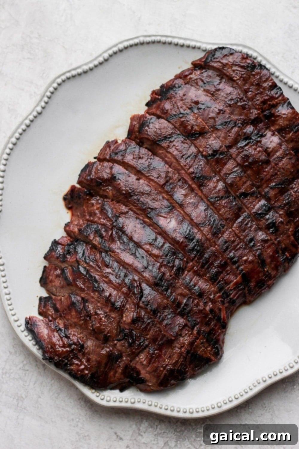 Flank steak is best served in thin strips! Cut against the grain of the meat and you will have perfect, tender strips for dinner! Grilled flank steak on a plate that is cut into strips, showcasing its tender texture.