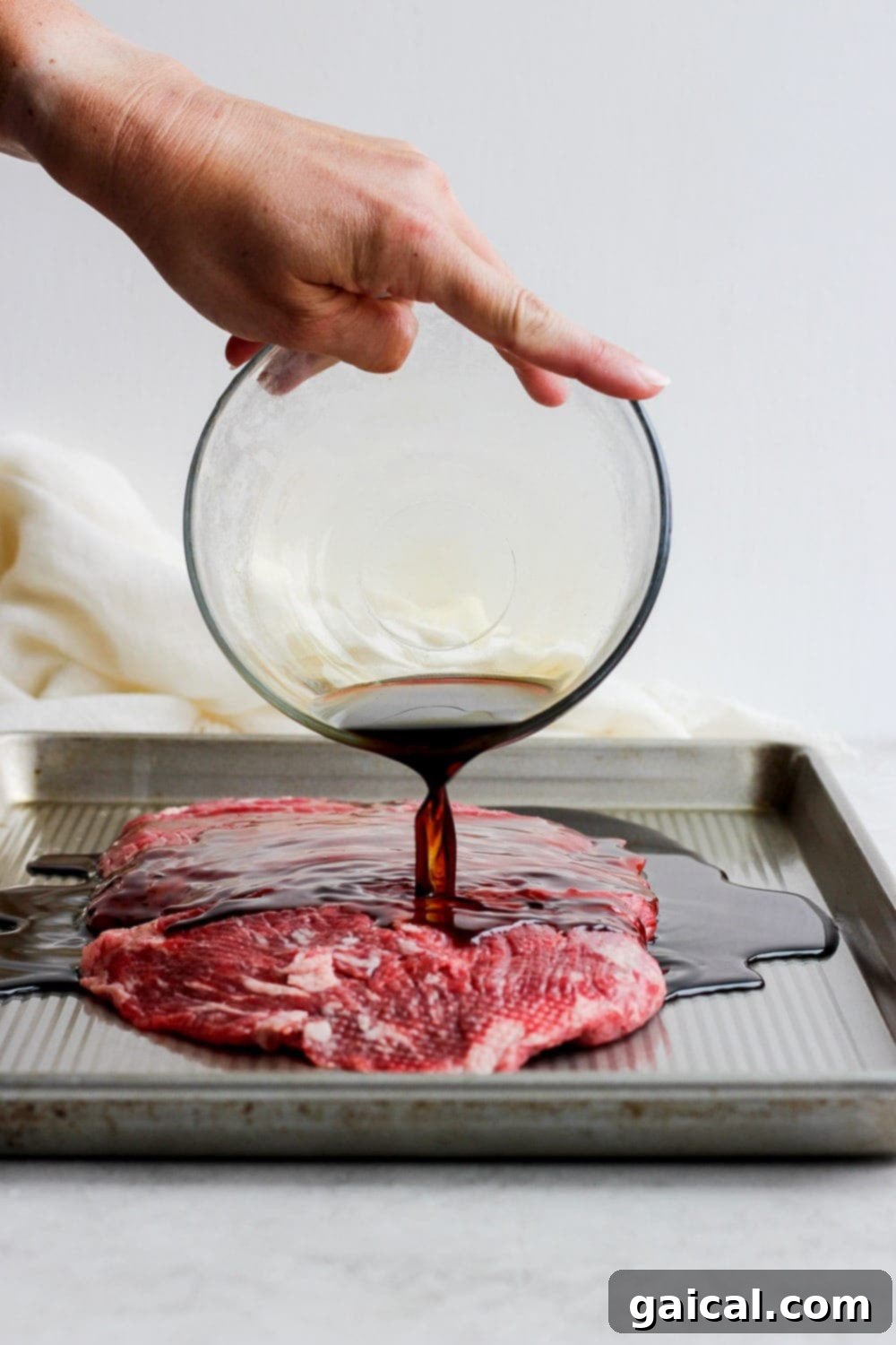 For a more flavorful grilled flank steak, marinate the meat in a delicious soy sauce marinade! You won't regret it! Pouring a rich marinade over a flank steak in a baking dish.