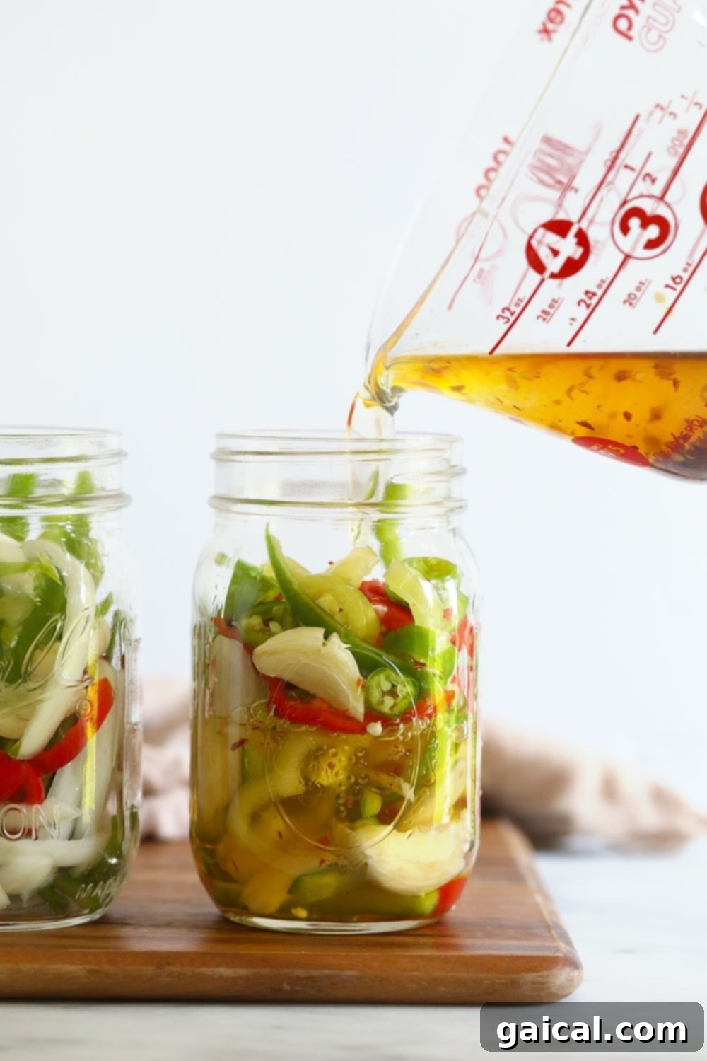 Sliced peppers and aromatics submerged in brine in a mason jar, mid-pickling process