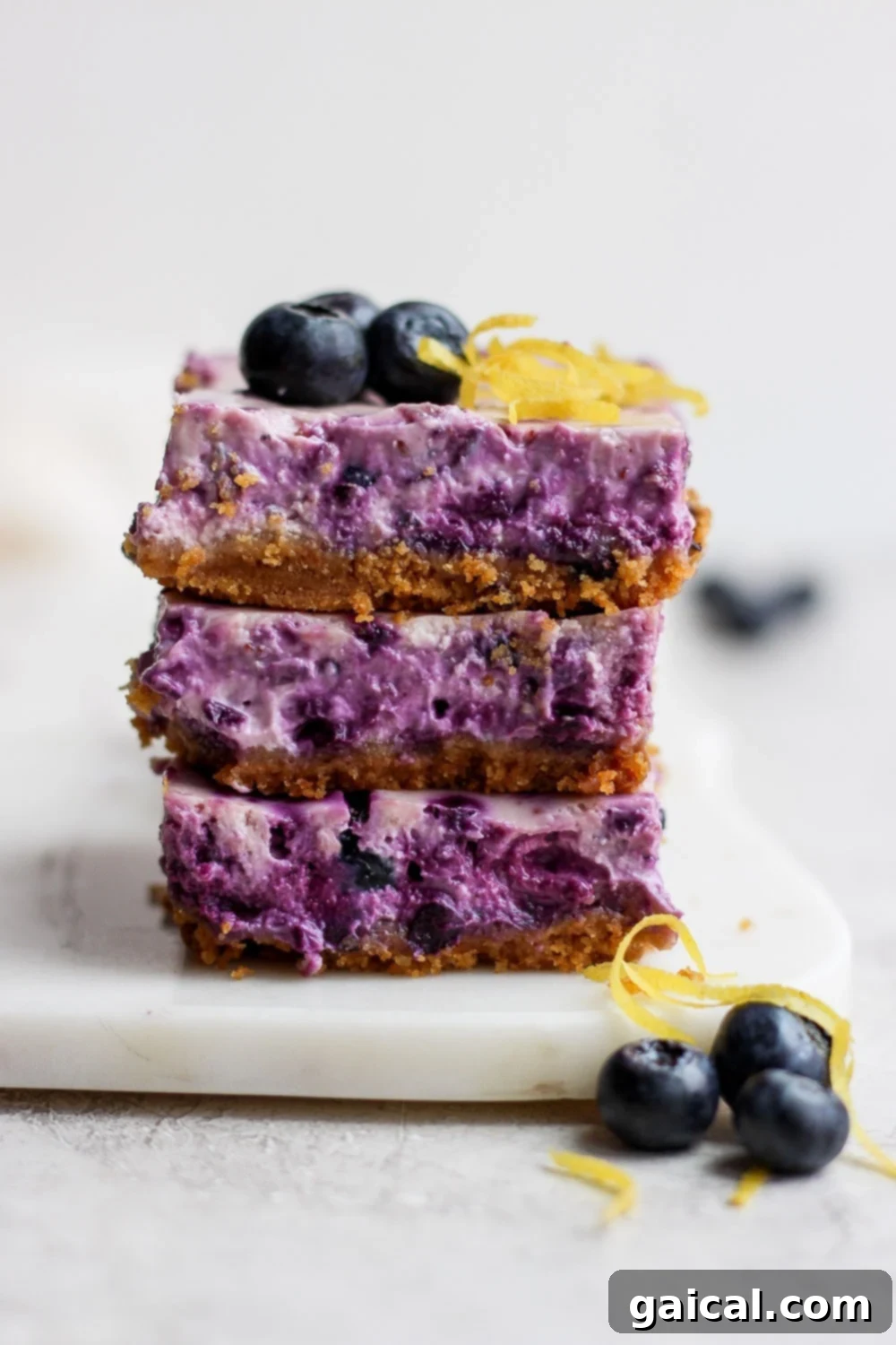 Three perfectly sliced blueberry cheesecake bars stacked on top of each other, showcasing their vibrant blue filling and golden crust, ready to be enjoyed.