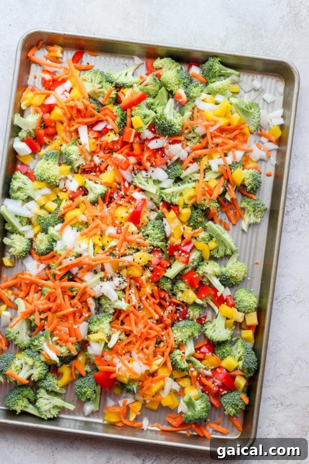 Sheet Pan Asian Salmon Bake 3 Freshly chopped broccoli, bell peppers, carrots, and onion on a sheet pan, drizzled with olive oil and seasoning, ready for roasting in the oven.