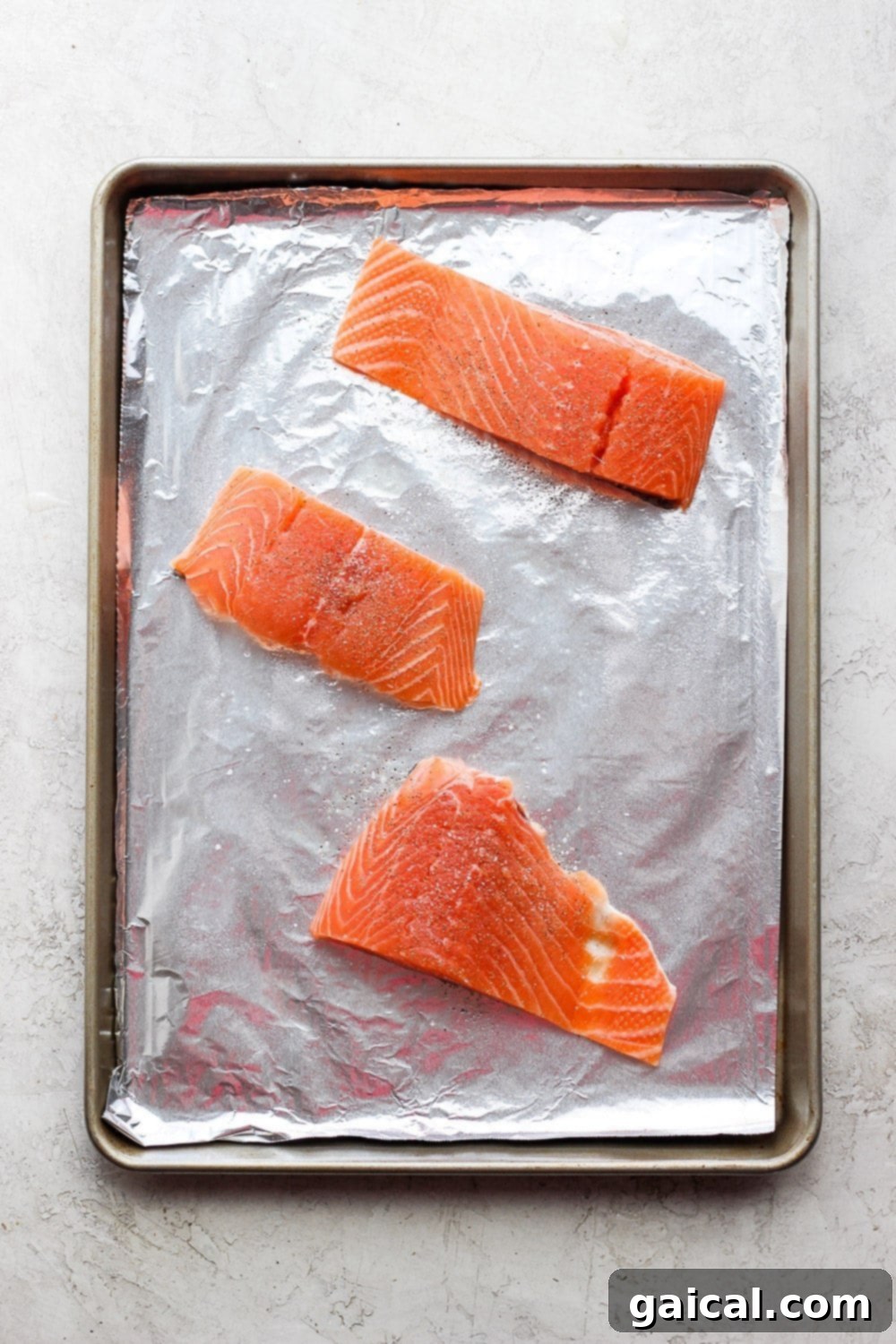 Sheet Pan Asian Salmon Bake 4 Two salmon fillets seasoned with salt and pepper, placed on a tin-foil lined baking sheet, ready for broiling in the oven.