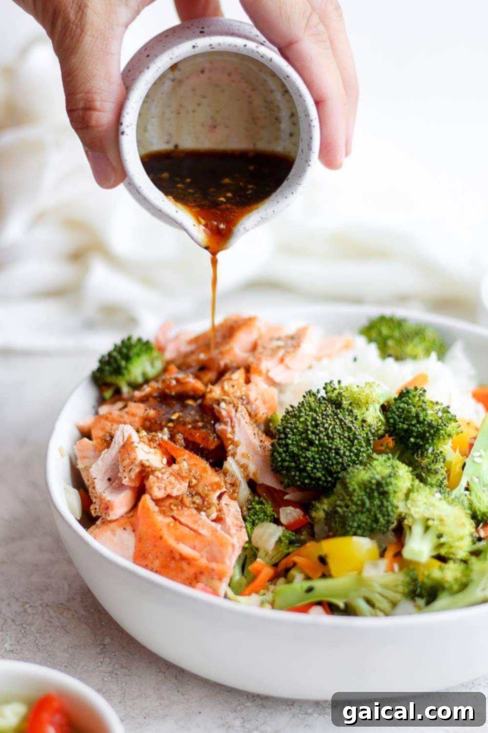 Sheet Pan Asian Salmon Bake 6 Heated stir fry sauce being poured generously over a bowl of sheet pan salmon stir fry with mixed roasted vegetables and flaky salmon.
