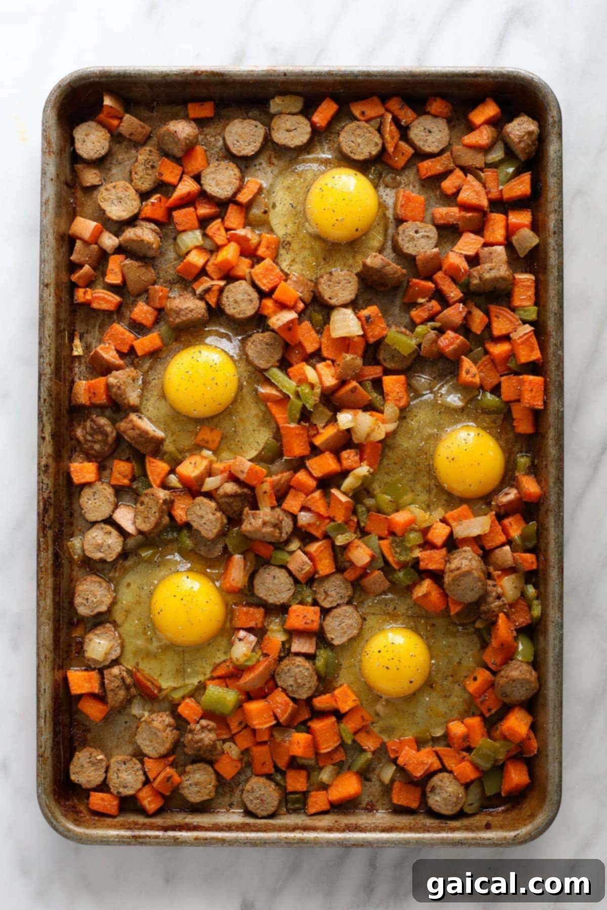 Sweet potato hash on a baking sheet with raw eggs cracked into individual nests, seasoned and ready for the oven.
