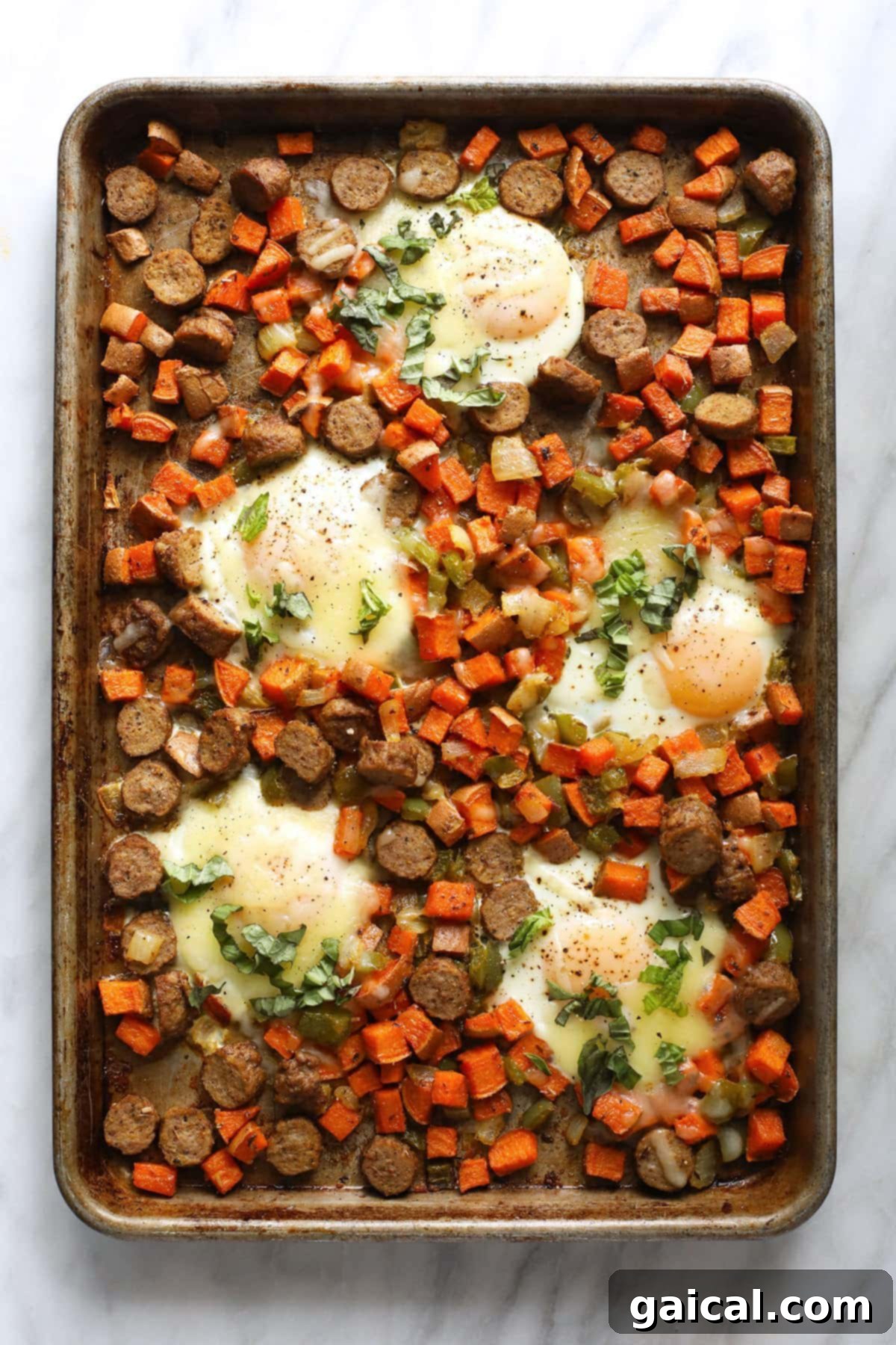 A completed sheet pan sweet potato hash with perfectly baked eggs, some with melted cheese, ready to be enjoyed.