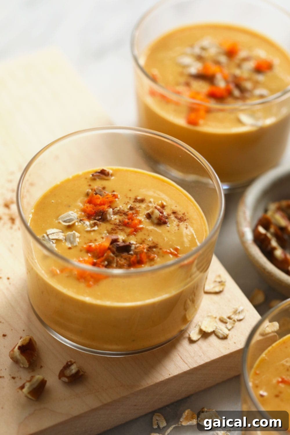 Two glasses of creamy carrot cake smoothie, garnished with a sprinkle of shredded carrots and cinnamon, presented beautifully on a light background.