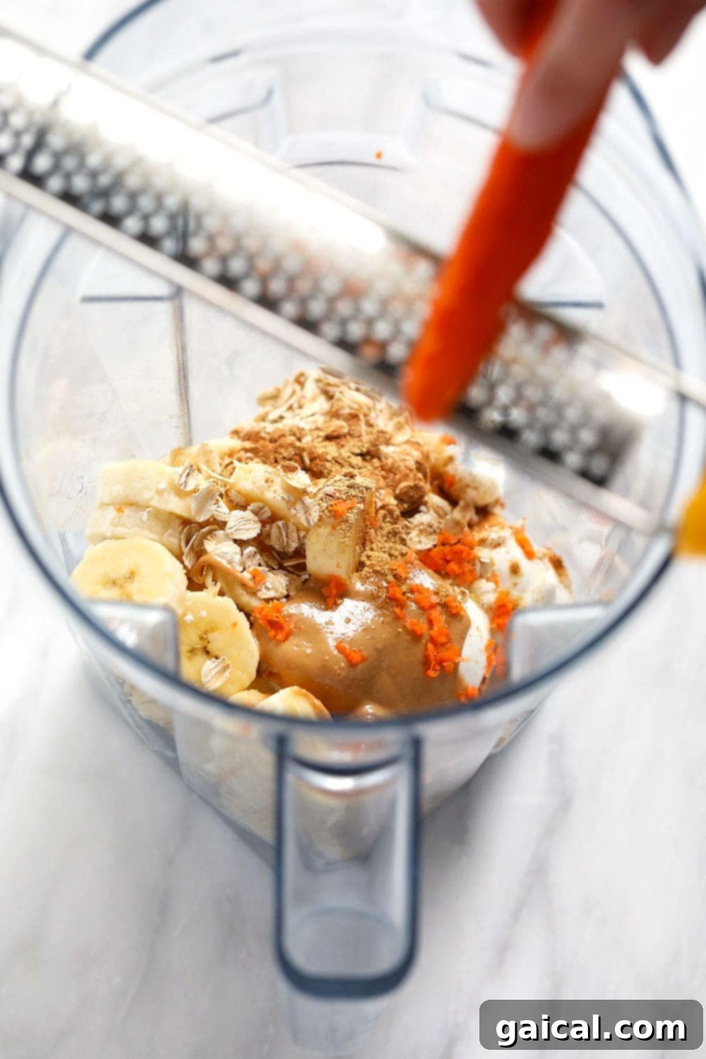 All the wholesome ingredients for a vibrant carrot cake smoothie, including frozen bananas, carrots, cashew butter, oats, and spices, are loaded into a high-speed blender, ready for blending.